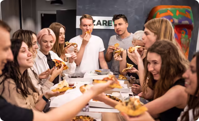 Group of young people enjoying pizza together around a table in a casual setting.