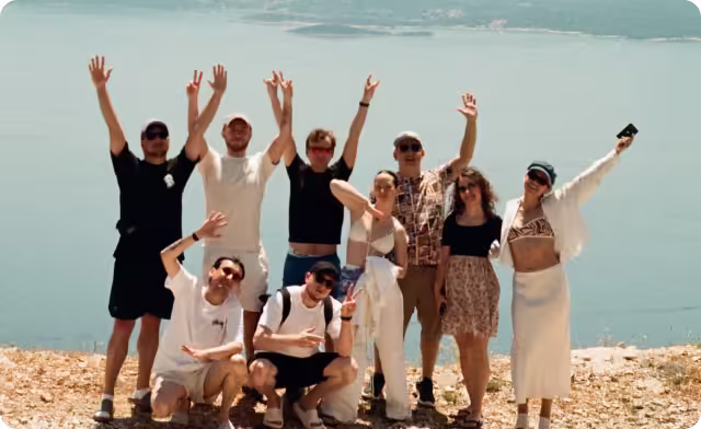 Group of nine people posing and smiling outdoors with water in the background.