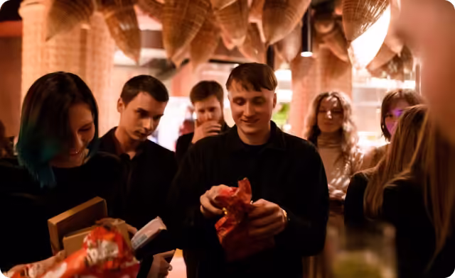 Group of people indoors unwrapping red gift packages under warm lighting.