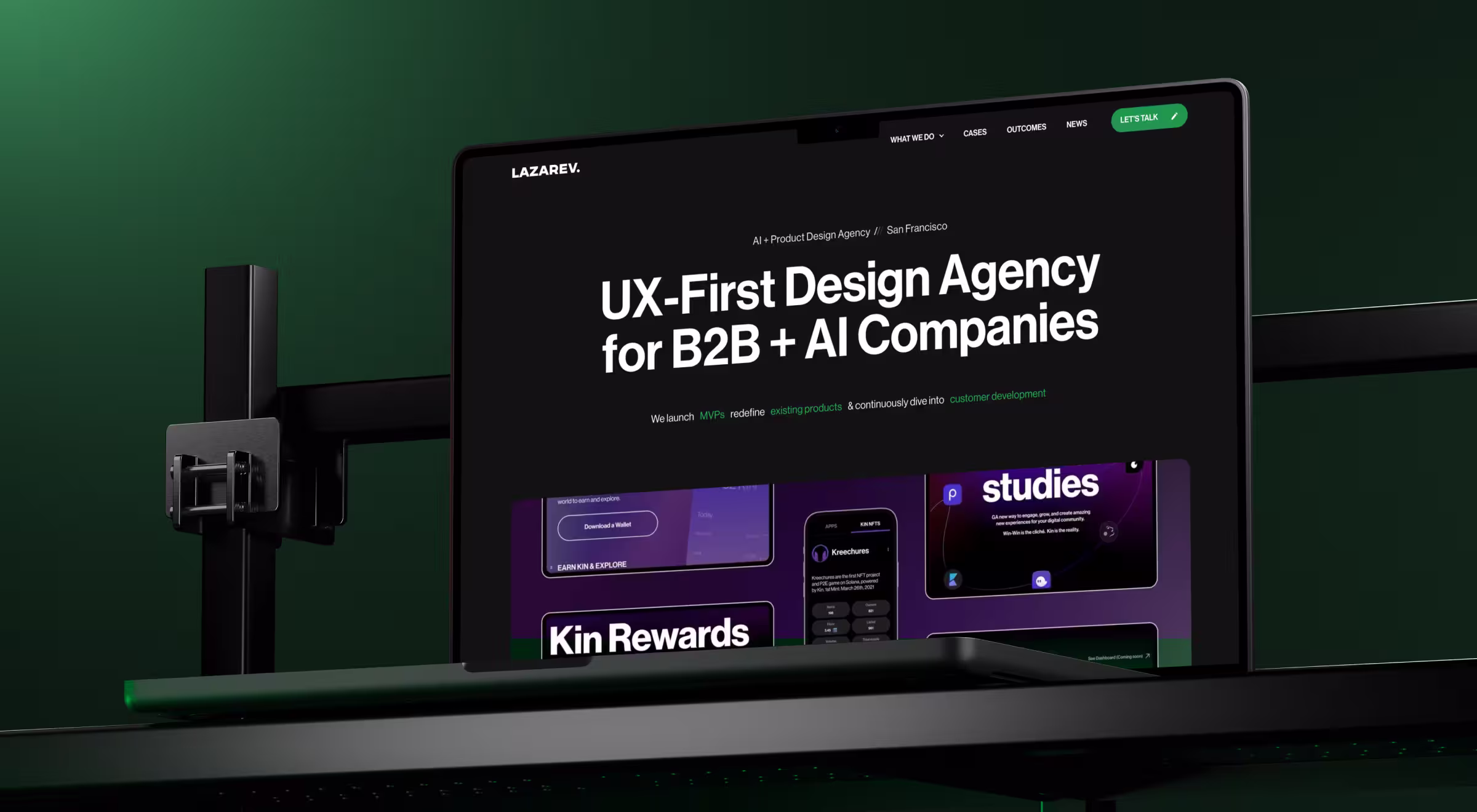 Laptop on a desk-mounted stand displaying the Lazarev.agency website, with the headline “UX-First Design Agency for B2B + AI Companies.” The interface uses a dark theme with green accents, a “Let’s talk” CTA in the top right, and case study thumbnails visible below the hero section against a green gradient background
