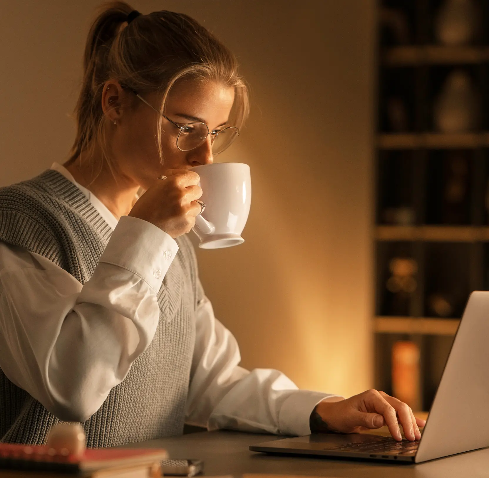 Person holding a mug while reviewing trading data on a laptop in warm evening light