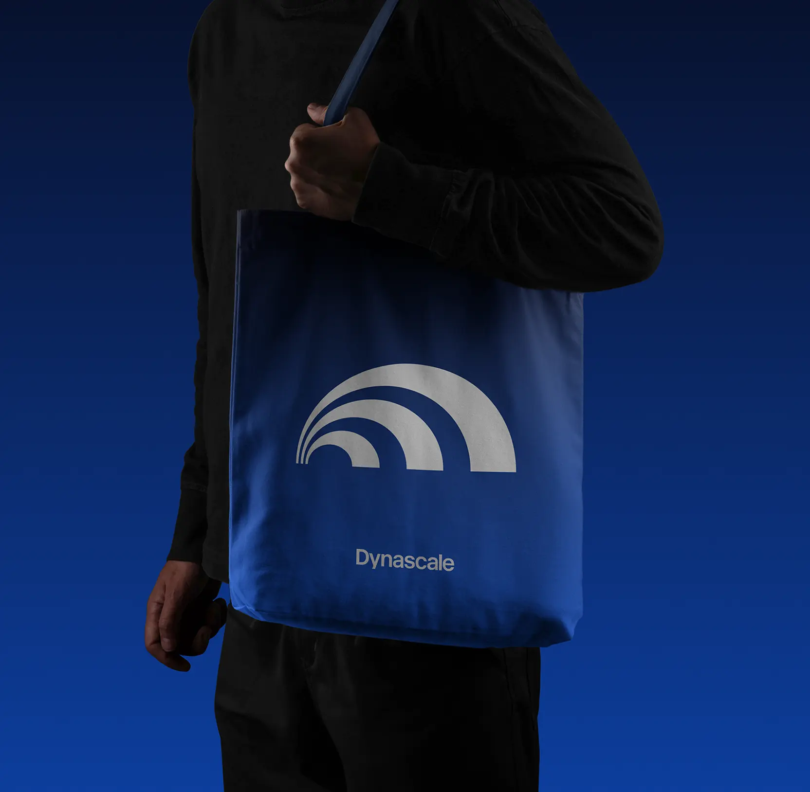 Person carrying a blue Dynascale tote bag with the arc mark and wordmark in white
