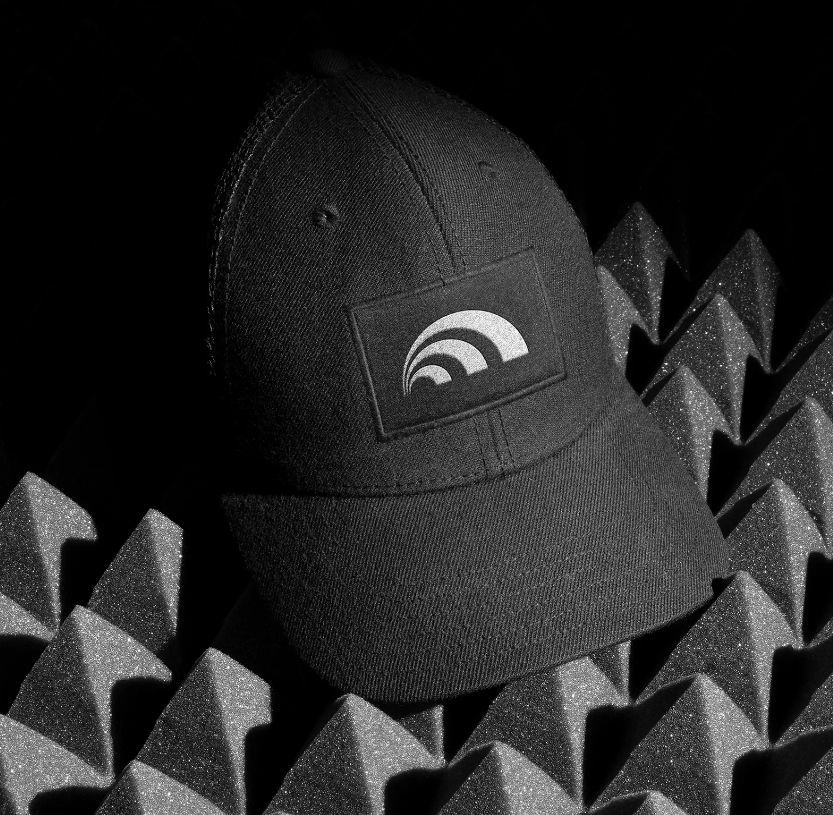 Black cap with an embroidered Dynascale arc patch, resting on acoustic foam