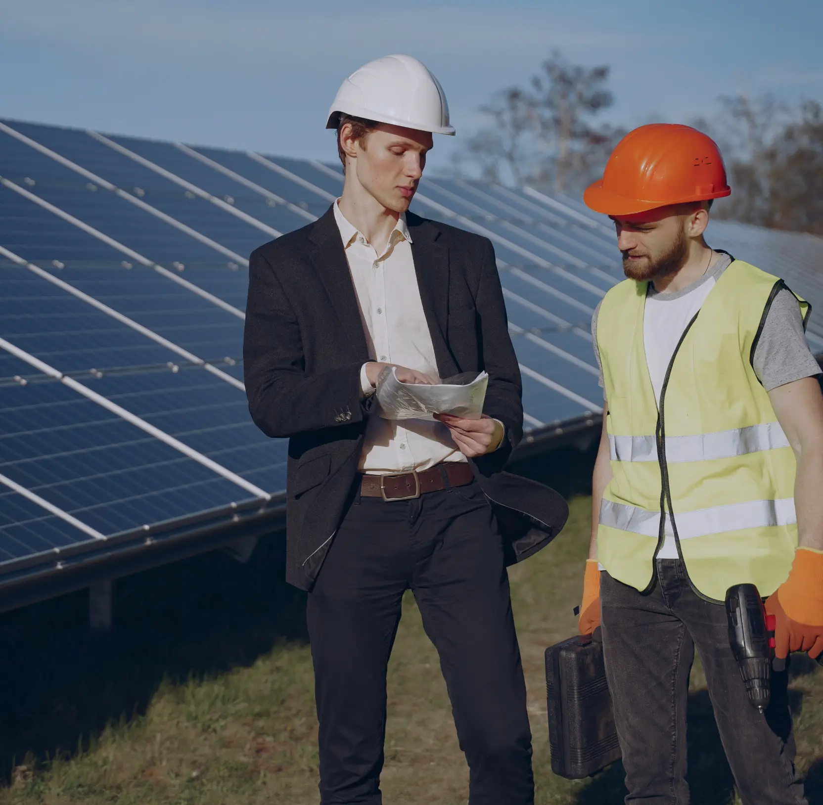 Two people in hard hats reviewing documents in front of a solar panel array
