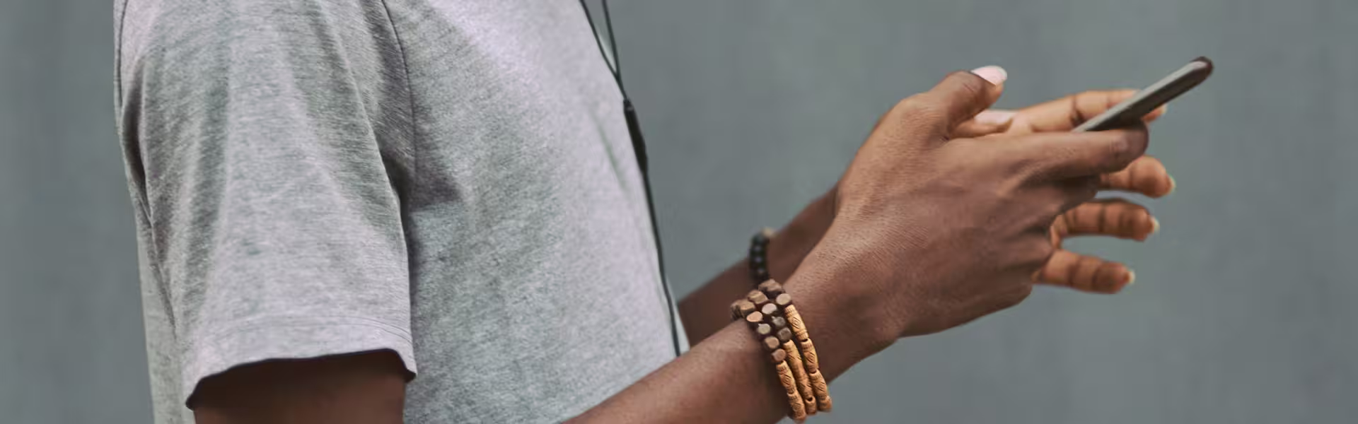 Close-up of a person using a smartphone while wearing casual clothes and bracelets, representing mobile interaction and digital connectivity