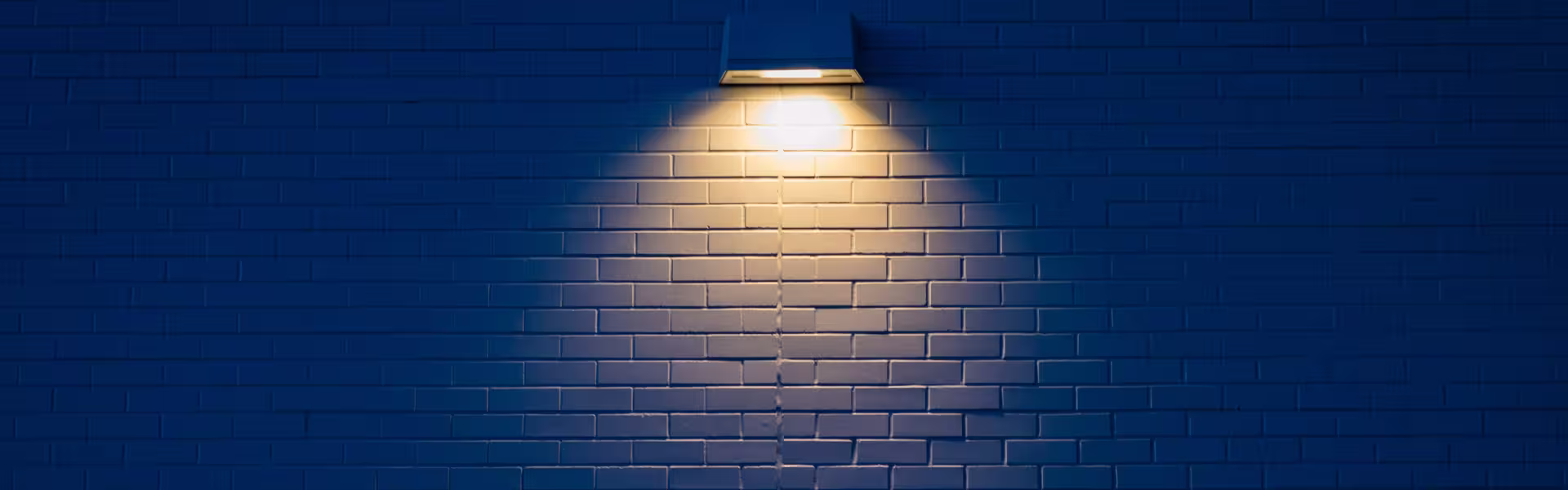 Wall lamp casting a warm spotlight on a blue brick wall, symbolizing standout UX design
