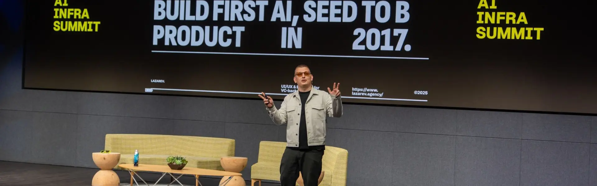 A speaker stands on stage at the AI Infra Summit, presenting in front of a large screen that reads: "100+ Awards Won. Build First AI, Seed to B Product in 2017."