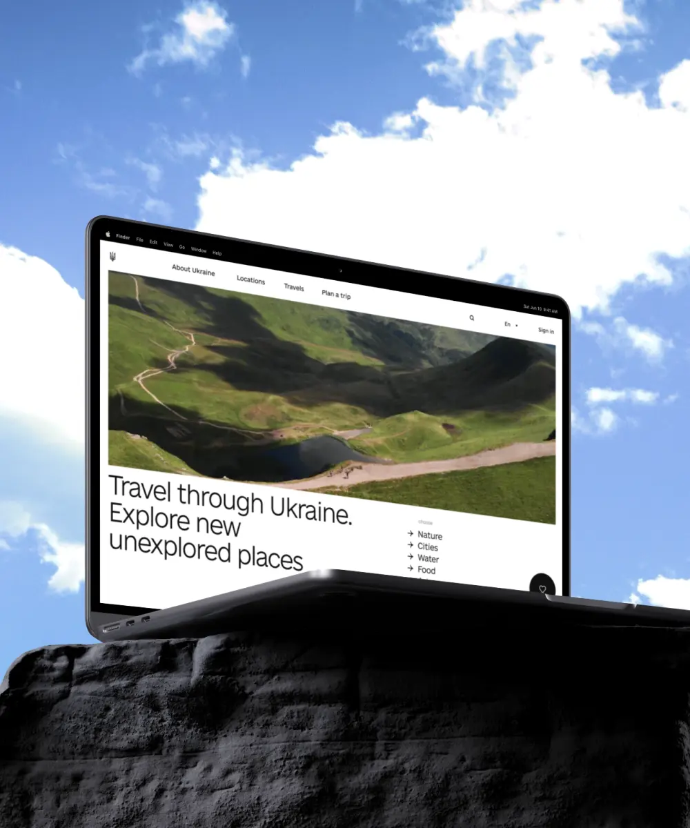 Laptop displaying a Ukraine travel and tourism website featuring scenic mountain landscapes, destination discovery categories, and trip-planning resources, positioned on a rocky surface against a bright sky backdrop to emphasize exploration and adventure.