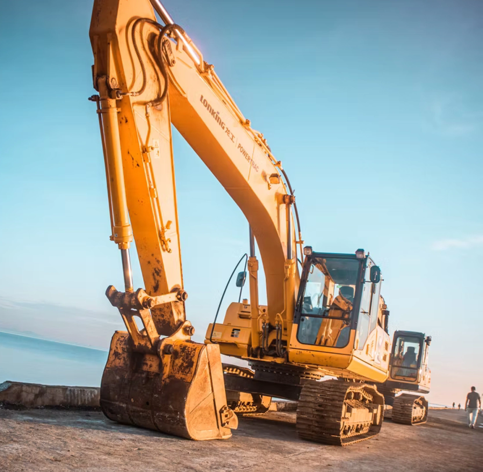 A yellow tracked excavator parked on open ground in warm sunset light, an example of the heavy equipment Shiplux transports.