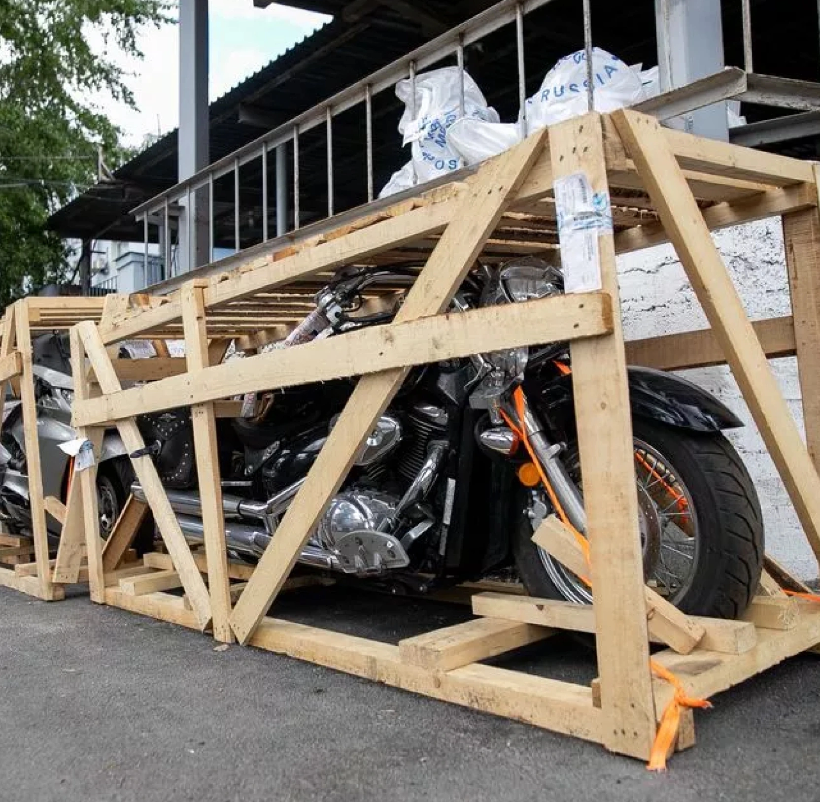 Two motorcycles secured inside custom wooden shipping crates on a street, showing protective crating for vehicle transport.