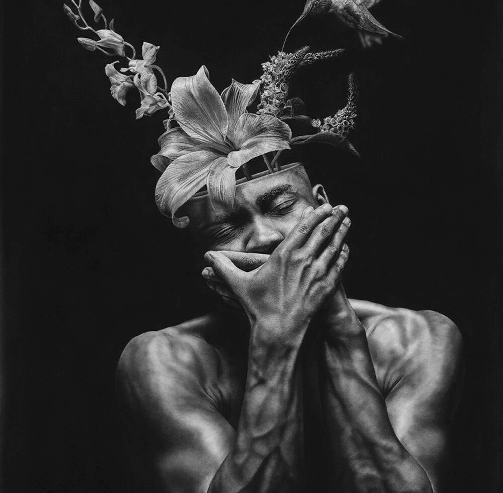 Black-and-white portrait of a shirtless man cradling his own face, with lilies, orchids and a hummingbird growing from the top of his head.